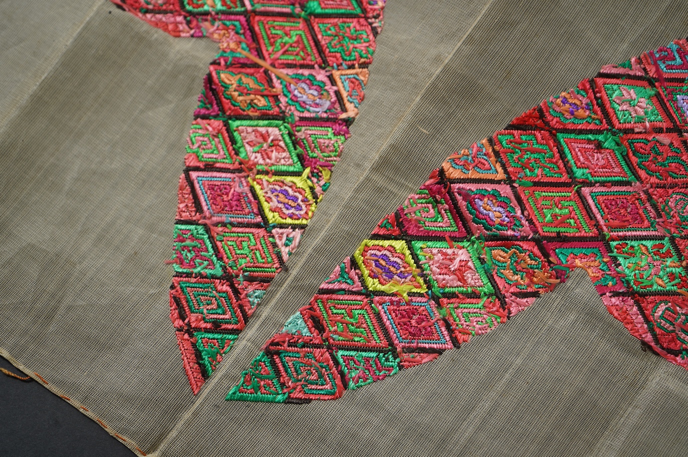 A pair of early 20th century Chinese silk polychrome finely embroidered slipper fronts, possibly from Guangxi province. Embroidered in a diamond grid, with stylistic and symbolic motifs. 21.5cm top to base. Condition - u